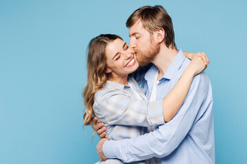 Side view young fun couple two friends family man woman wear shirt casual clothes together hug cuddle kiss cheek isolated on pastel plain light blue cyan background studio portrait. Lifestyle concept.