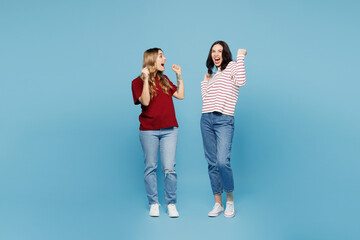 Fototapeta premium Full body young happy couple two friends women wear red casual clothes together do winner gesture celebrate clenching fists say yes isolated on pastel plain light blue background. Lifestyle concept.