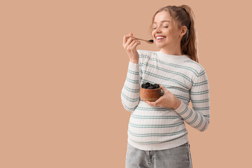 Young pregnant woman eating dried prunes on beige background