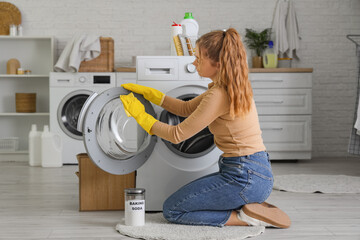 Young woman cleaning washing machine with baking soda in laundry room