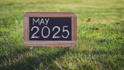 Chalkboard with text MAY 2025 on green in park. Spring season.