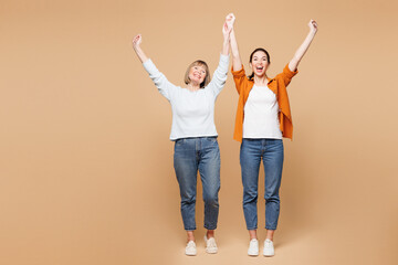 Fototapeta premium Full body elder parent mom 50s years old with young daughter two women together wearing casual clothes do winner gesture celebrate clenching fists isolated on plain beige background Family day concept
