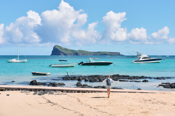 Obraz premium A young woman strolls along a stunning beach with a view of the iconic Coin de Mire Island, Mauritius