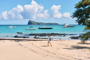 A young woman strolls along a stunning beach with a view of the iconic Coin de Mire Island, Mauritius