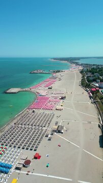 Eforie Nord Beach, Romania, aerial perspective. Drone going forward. Season time, beach full with sunshades. People at the beaches. Turquoise water. Famous travel destination.