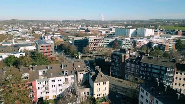 Aerial footage of Aachen showcasing residential homes, modern office buildings, and industrial zones. Cityscape is framed by rolling hills under bright blue sky. Location: Aachen, Deutschland Germany