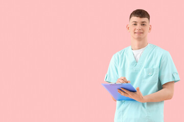 Male medical intern writing in clipboard on pink background
