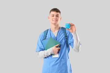 Male medical intern with notebooks and pill box on light background
