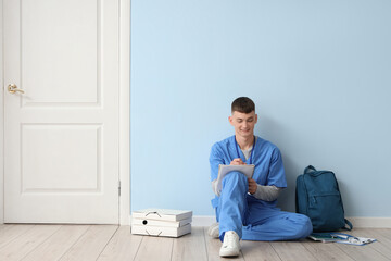 Male medical intern writing in notebook near blue wall