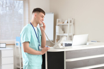 Male medical intern talking by telephone at reception desk in clinic