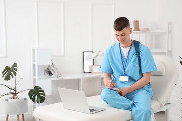 Fototapeta premium Male medical intern studying with laptop in clinic