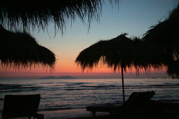 Stunning sunset over the Albanian coastline with silhouettes of palm trees and tranquil waves lapping at the shore
