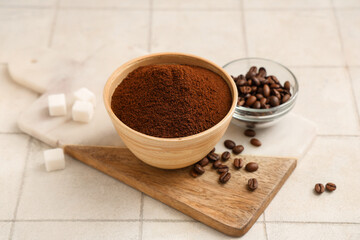 Board with bowl of coffee powder, beans and sugar cubes on white tile background