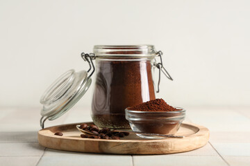 Wooden board with jar of coffee powder, beans, bowl and spoon on white tile table