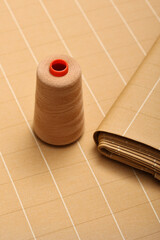 Top down flat lay photo of beige, plaid, wool, fashion fabric on designers table. Sewing thread on top of the fabric.