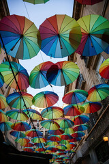 Colorful umbrellas create a vibrant canopy over a charming street in a lively urban area during sunset hours