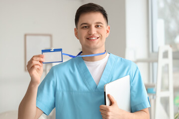 Male medical intern with badge and laptop in clinic