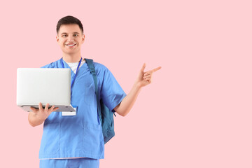 Male medical intern with laptop pointing at something on pink background