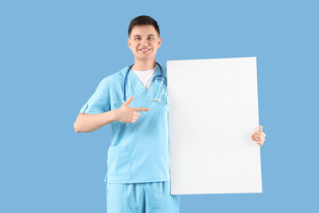 Male medical intern pointing at blank poster on blue background