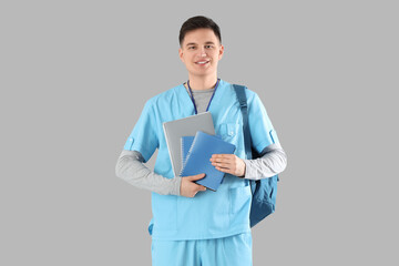 Male medical intern with backpack and notebooks on grey background
