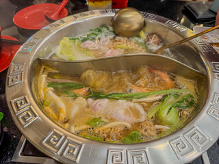 Steaming hot pot filled with vegetables and seafood at a busy diner setting