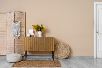 Vase with mimosa flowers and decor on chest of drawers near beige wall in living room interior