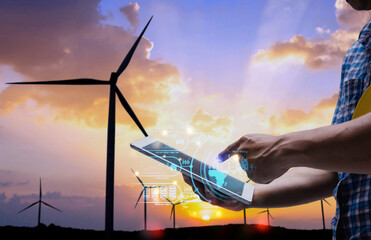 A person uses a tablet with digital interface to monitor wind turbines at sunset, symbolizing renewable energy and smart technology.