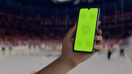 GREEN SCREEN CHROMA KEY A hand holding a phone with a green screen at a hockey game in an indoor stadium, ideal for showcasing live sports or betting apps