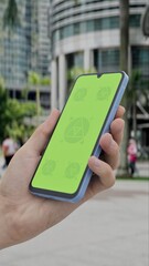 GREEN SCREEN CHROMA KEY Smartphone with green screen held in hand in an urban cityscape with palm trees and buildings, perfect for app or tech displays