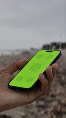 GREEN SCREEN CHROMA KEY Person holding a smartphone at a scenic beach during sunset with silhouettes of people and waves in the background