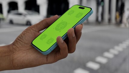 N SCREEN CHROMA KEY Person holding a smartphone with a green screen on a city street, showcasing...