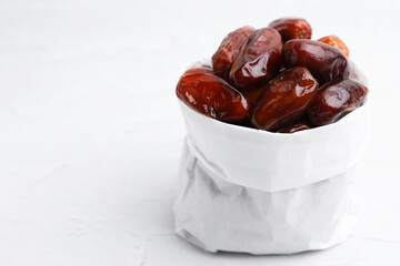 Tasty sweet dried dates in paper bag on white table, closeup. Space for text