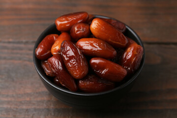 Tasty dried dates in bowl on wooden table, closeup