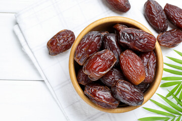 Tasty dried dates and leaves on white wooden table, flat lay