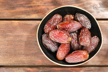 Many tasty dried dates in bowl on wooden table, top view. Space for text