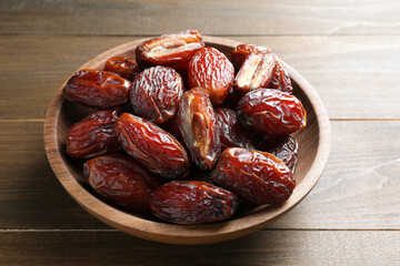 Many tasty dried dates in bowl on wooden table, closeup
