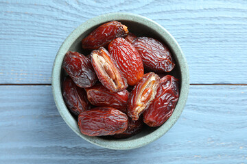 Many tasty dried dates in bowl on blue wooden table, top view