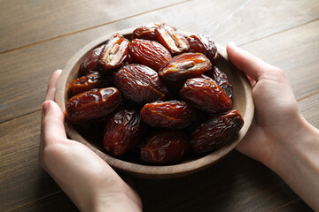 Woman with bowl of tasty dried dates at wooden table, closeup