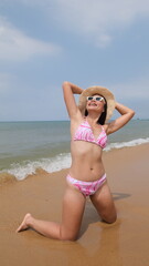 Basking in the sun, pretty Asian woman wears a pink and white patterned bikini and a straw hat with white sunglasses