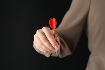 Woman holding dart on black background, closeup