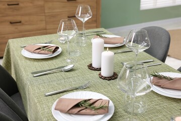 Stylish table setting with olive tablecloth, glasses and candles indoors