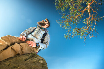 Directly below portrait of stylish man with a beard, wearing outdoor clothing, sunglasses, and a...