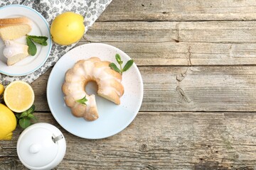 Delicious lemon cake with glaze, mint and citrus fruits on wooden table, flat lay. Space for text