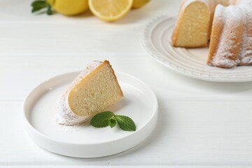 Piece of delicious lemon cake with powdered sugar and mint on white wooden table