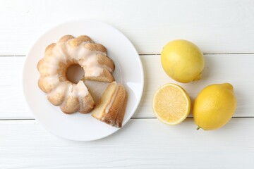 Delicious lemon cake with glaze and citrus fruits on white wooden table, flat lay
