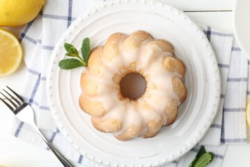 Delicious lemon cake with glaze, mint and citrus fruits on white wooden table, flat lay