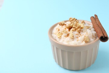 Tasty rice pudding with walnuts and cinnamon on light blue background, closeup. Space for text