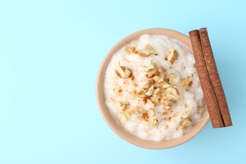 Tasty rice pudding with walnuts and cinnamon on light blue background, top view. Space for text