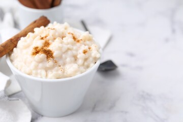 Tasty rice pudding with cinnamon served on white marble table, closeup. Space for text