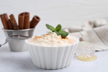 Tasty rice pudding with cinnamon and mint on light grey table, closeup